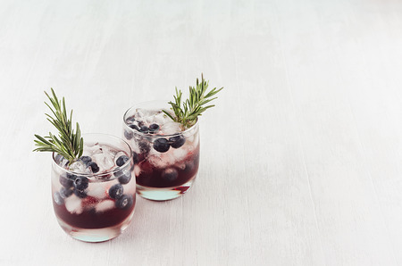 Juicy arctic traditional cold cocktails with ice cubes, blueberry, rosemary in wet glasses on white wood board, top view, copy space.の写真素材