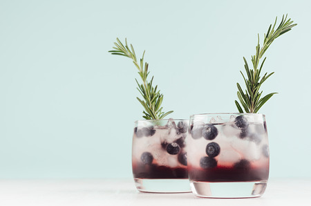 Summer fresh blueberry cocktails in glasses with berry, ice cubes, rosemary on white wood table and pastel mint color wall, copy space.の写真素材