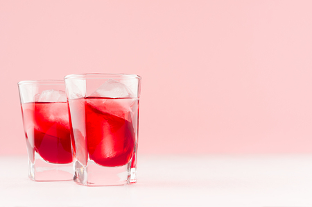 Red alcoholic liquor shots with ripe slice of strawberry with ice cubes on pastel soft light pink background, copy space.の写真素材