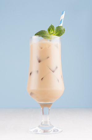 Fresh summer ice coffee in wet exquisite transparent glass with ice cubes, straw, green mint in light blue interior, vertical.の写真素材