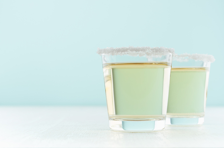Tropical fresh alcohol yellow drink - golden tequila in two shot glasses with rim of salt in elegant pastel green color kitchen interior, copy space.の写真素材