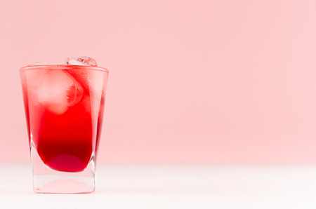 Fresh summer strawberry homemade lemonade in shot glass with ice cubes in elegant pastel pink color...