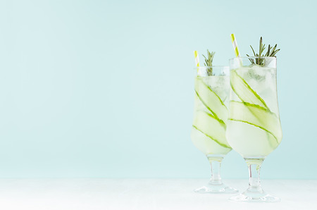 Tropical fresh summer homemade lemonade in two glasses with ice cubes, cucumber, rosemary, lime, straw in elegant pastel green color kitchen interior.の写真素材