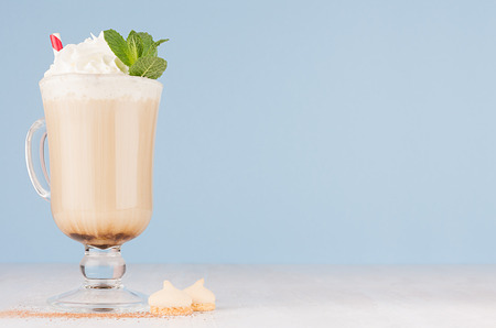 Fresh coffee drink with whipped cream, green mint, straw, cookies in irish coffee glass on soft light blue wall and white wooden table, copy space.の写真素材