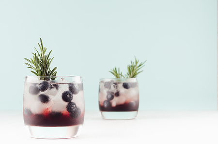 Tropical alcoholic shots of sweet berry liquor with ice cubes, blueberry, rosemary on pastel soft light green background, copy space.の写真素材