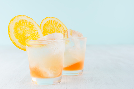 Fresh oranges striped cocktail with liquor, sliced orange, ice cubes on elegant soft blue color wall and white wooden table.の写真素材