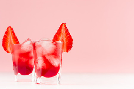 Fresh summer strawberry homemade cocktails in two shot glasses with ice cubes, strawberry slice in elegant pastel pink color kitchen interior.の写真素材
