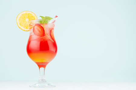 Summer oranges alcohol drink sunrise with orange, ripe sliced strawberry, ice cubes, mint in misted wineglass on blue background.の写真素材