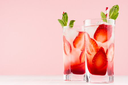 Healthy cold fruit beverage with strawberry and mineral water, mint, ice, straw in modern elegant pastel pink interior, copy space.の写真素材