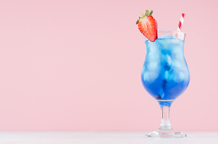 Tropical beach alcohol blue drink  - curacao liquor, strawberry slice, ice, straw in misted glass on pink background, white wood board.の写真素材