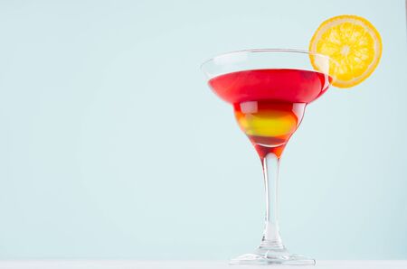 Alcohol cocktail for celebration  with red and yellow liquor, orange slice in mint color bar interior on white wood table.の写真素材