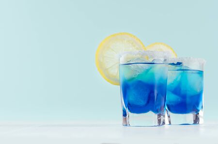 Exquisite blue cocktails for celebration in beach style with blue curacao, ice cube, sugar rim, lemon slice in mint color bar interior on white wood table.の写真素材