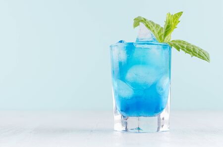Tropical fresh alcohol cocktail with blue curacao liqueur, ice cube, green mint in frozen shot glass on soft light white, pastel green background.の写真素材