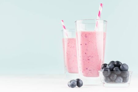 Violet fresh milk dessert with blueberries in bowl, striped straw in modern youth interior in pastel soft mint color and white wood table, copy space.の写真素材