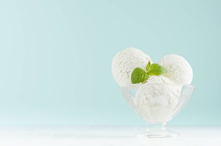 Summer cold dessert - three creamy ice cream balls in elegant glass bowl with green mint on white wood table and pastel blue wall.の写真素材