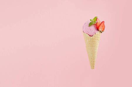 Flavor pink ice cream in crisp waffle cone with strawberry slices, green mint leaf on pink background, copy space.の写真素材