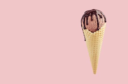 Brown ice cream in crisp waffle cone with chocolate sauce on pastel pink background, mock up for...