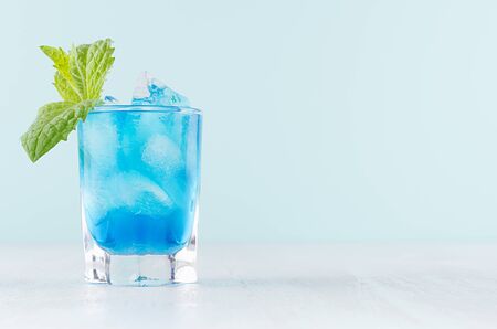 Cool summer blue beverage margarita for party with ice cubes, green mint on white wood board and mint color wall.の写真素材