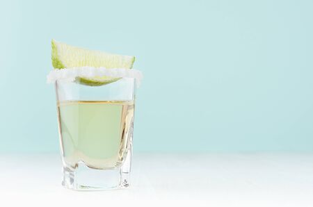 Cool summer beverage for party - tequila with salt rim and green lime on white wood board and mint color wall.の写真素材