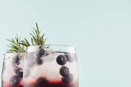 Tropical alcoholic shots of sweet berry liquor with ice cubes, blueberry, rosemary on pastel soft light green background, closeup, top section.の写真素材