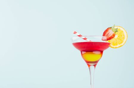 Homemade tropical fruit cocktail  with red and yellow liquor, orange slice, strawberry, straw in fresh mint color background, closeup, details, top.の写真素材
