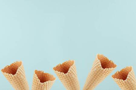 Summer food decorative border of empty waffle ice cream cones on soft light green background, copy...