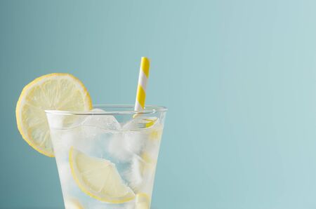 Cold shine sparkling refreshing drink for party with lemon slices, ice cubes, tonic, yellow straw in...