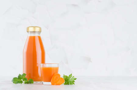 Fresh vegetable orange carrot juice in glass bottle with blank label mock up with glass, green parsley, slices in soft light white interior on wood table.の写真素材