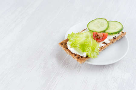 Organic season sandwiches on dry brown grain crispbread with fresh sliced vegetables - green salad, cucumber, tomato, cream cheese on white wooden table, closeup, copy space.の写真素材
