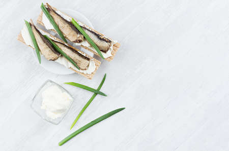 Healthy dietary breakfast of whole grain wheat crisps breads with anchovies, cream cheese, green onion sprout on white wood background, top view, copy space.の写真素材