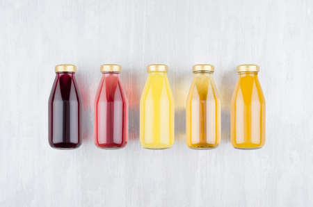 Organic fruits juices - set of different color juices with cap in glass bottles on white wood...