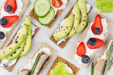 Summer light sweet open sandwiches on crisps bread with vegetables, ripe fruits, fish preserves,...
