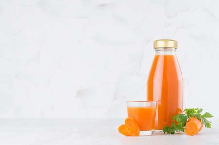 Fresh vegetable orange carrot juice in glass bottle template with glass, green parsley, slices on wood table and white background with copy space.の写真素材