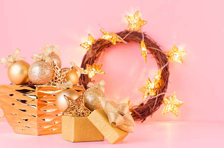 Christmas background in gold glitter color - christmas wreath, balls, gift box and glowing stars lights on light pink background, copy space.の写真素材