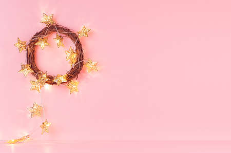Christmas wreath with gold shimmer glowing stars garland on soft light pastel pink background, copy...