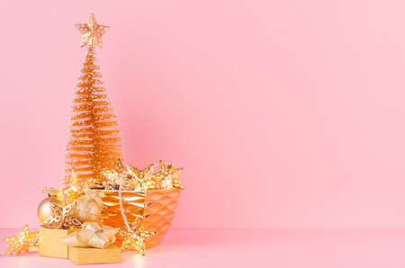 Gold christmas tree with glowing stars lights, balls in bowl, present on elegant pastel pink...