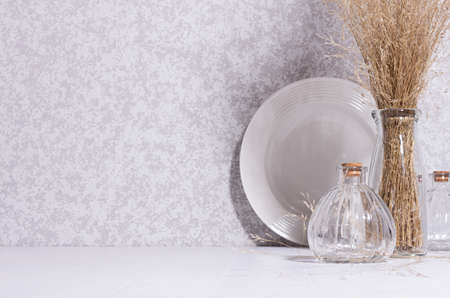 Simple elegant hygge home decor with white ceramic dish, glass bottles and bouquet of dried grass on...