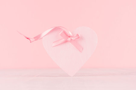 Gentle decor for Valentine days - soft light pink heart with ribbon on white wood board, closeup.の写真素材