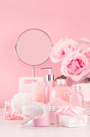 Modern youth bathroom or dressing table design in pastel pink color - fresh pink flowers, cosmetic products, bath accessories, jewelry, round mirror on white wood board.の写真素材