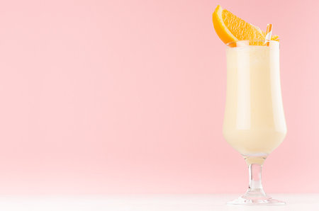 Bright oranges milkshake in elegance glass with slices orange on white wooden table and pastel light pink wall.の写真素材