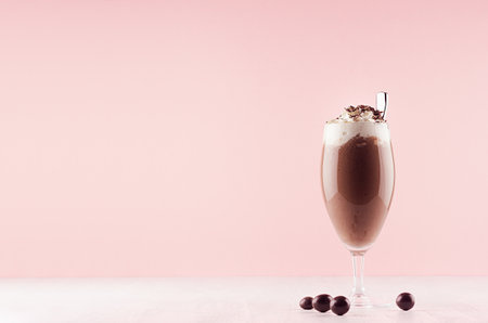Chocolate fresh shake in graceful glass with candies, whipped cream, chocolate chips and straw on pink background.の写真素材