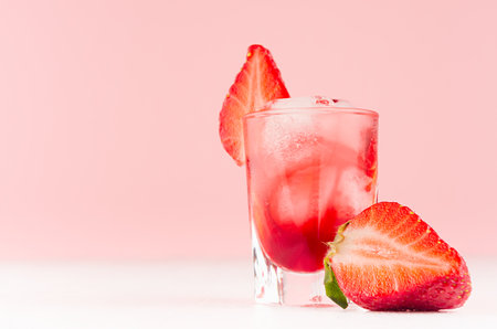 Summer fresh red strawberry drink with ice cubes and slice berry on fashion pastel pink color background and white wood table, copy space.の写真素材