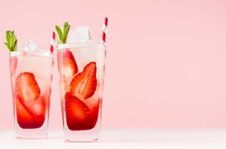 Fresh strawberry cocktails with slices fruits, mint, straw, ice cubes in misted glass on white wood table and pink color wall.の写真素材