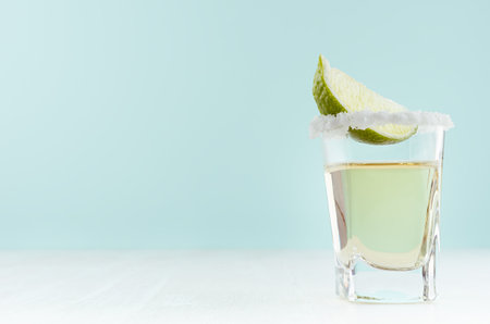 Tequila cocktail with fresh piece lime, rim of salt in shot glass on white wood table and blue color wall, copy space.の写真素材