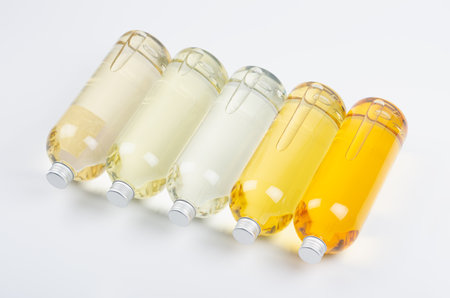 Collection transparent lying bottles with different pale colors liquid, cosmetic product, perfume or drink and silver cap in diadonal row on white background, top view.の写真素材