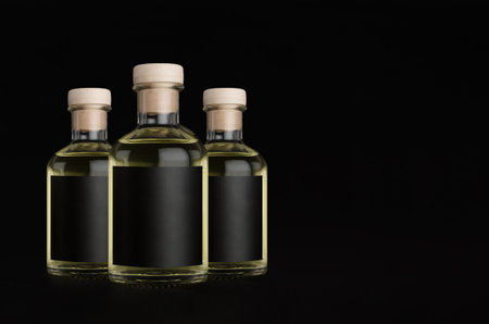 Elegant three glass bottles for cosmetic, perfume, drink with black label, cork, liquid on black background, mock up for design, copy space.の写真素材