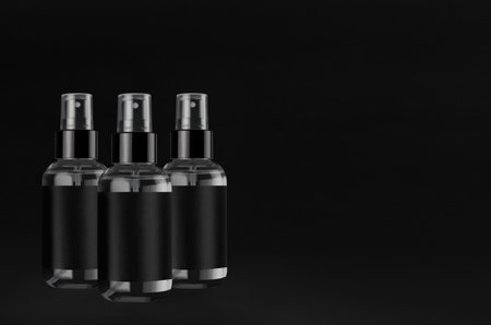 Small three exquisite transparent spray dispenser bottles for cosmetics with black label on black background, mock up for design, copy space.の写真素材