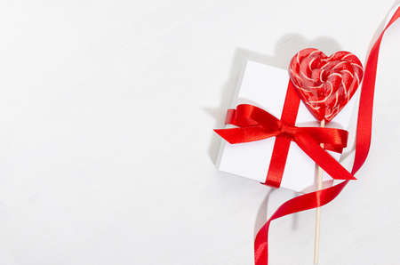 Classic elegant festive background with love - white gift boxes with red bow, curl ribbon, sweet lollipops hearts on white wood board, border, copy space.の写真素材