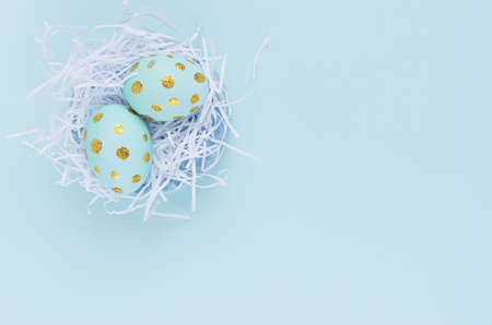 Stylish easter background - blue easter eggs with gold dots in white nest on blue color, top view.