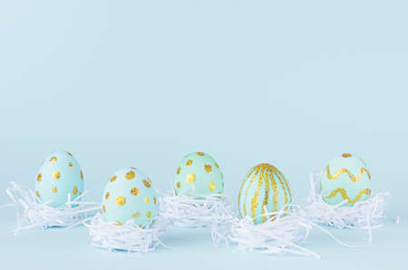 Festive easter background - blue easter eggs with golden glitter design in bow in white nest on...